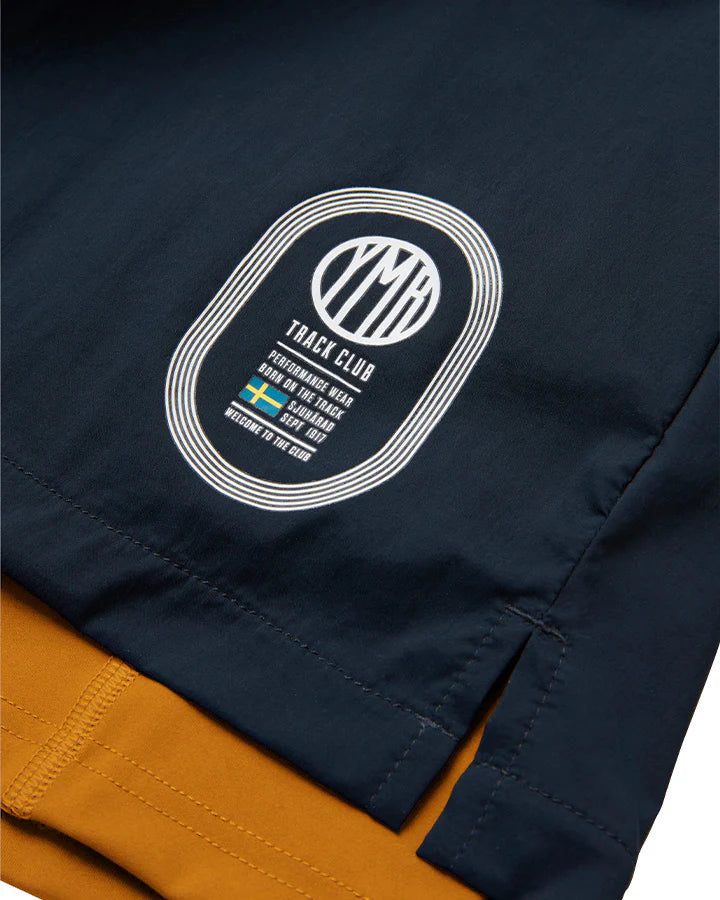 Marinblå 2-1 shorts med ett ytterlager av lätt funktionsmaterial. Under finns ett par gula kompressionstights med sidfickor på båda benen. Vit logotyp på framsidan, vänster ben. Midjebandet säkras med invändig snörning.