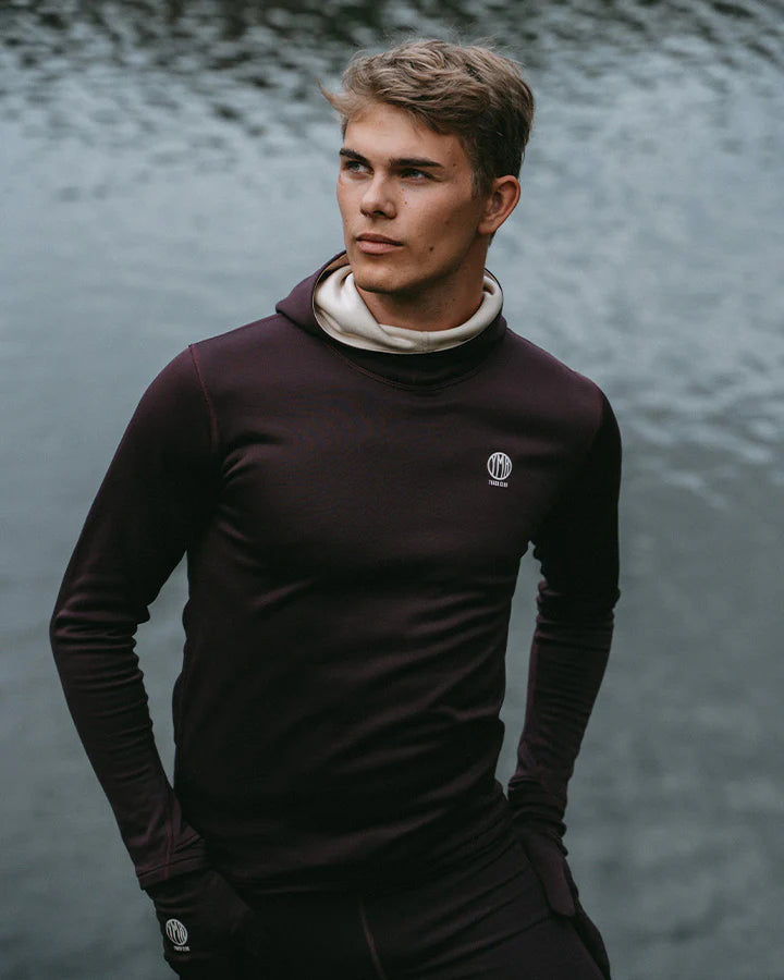 YMR Åsunden Men's Hoodie. Hoodie i rödbrun nyans med beige kontrastfärg på insidan av luvan och på loggan på bröstet. Huva med hög krage och tumöppningar i ärmsluten. Tight, sportig passform.