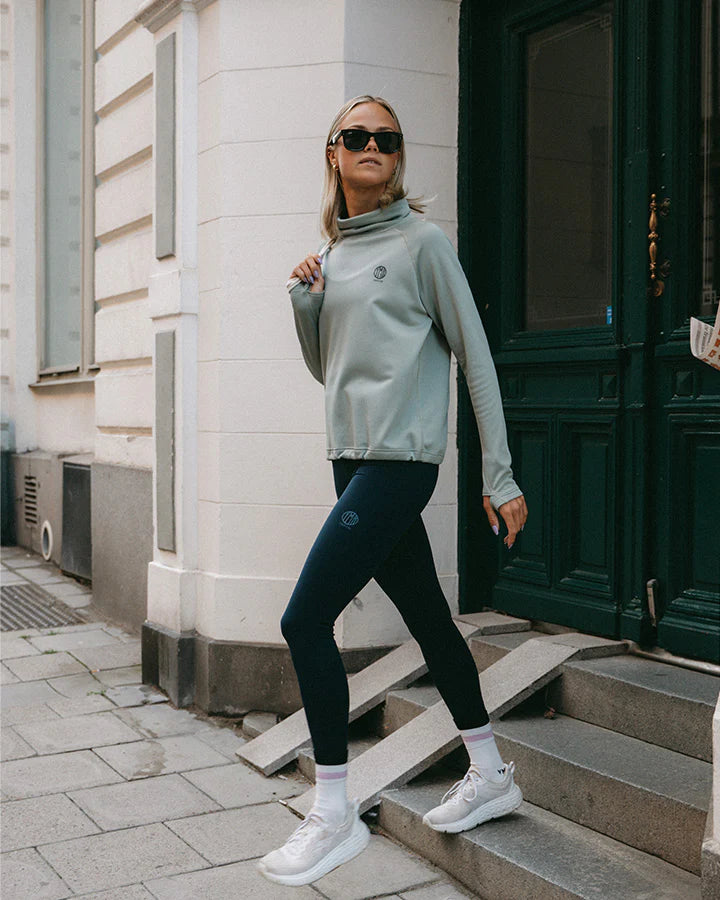 YMR Åsunden Ladies Funnel Neck Mint. Ljusgrön mångsidig och mjuk tröja med mörkblått inuti den höga kragen och på logotyp på bröstet. Dragsko i både kragen och i midjan för justerbar passform. Reflexdetalj på nedre delen av ryggen.