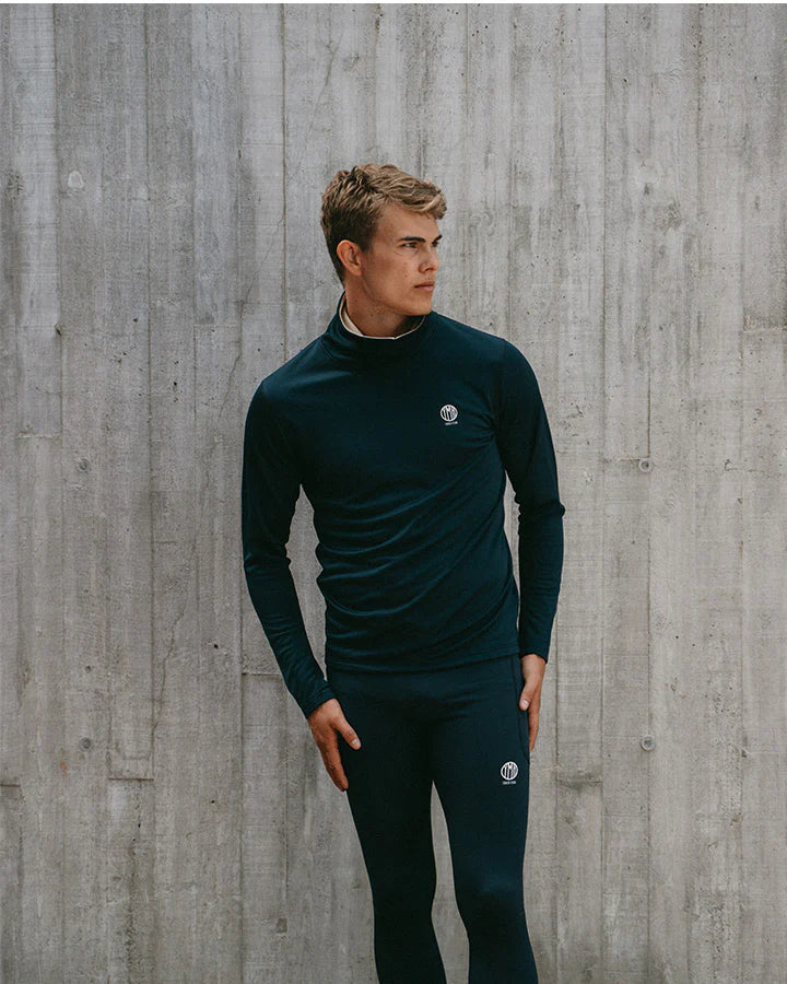 YMR Åsunden Men's Funnel Neck Navy. Mångsidig och mjuk tröja i marinblått med beige inuti den höga kragen och på logotyp på bröstet. Dragsko i både kragen för justerbar passform. Reflexdetalj på nedre delen av ryggen.