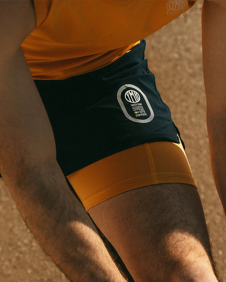 Marinblå 2-1 shorts med ett ytterlager av lätt funktionsmaterial. Under finns ett par gula kompressionstights med sidfickor på båda benen. Vit logotyp på framsidan, vänster ben. Midjebandet säkras med invändig snörning.