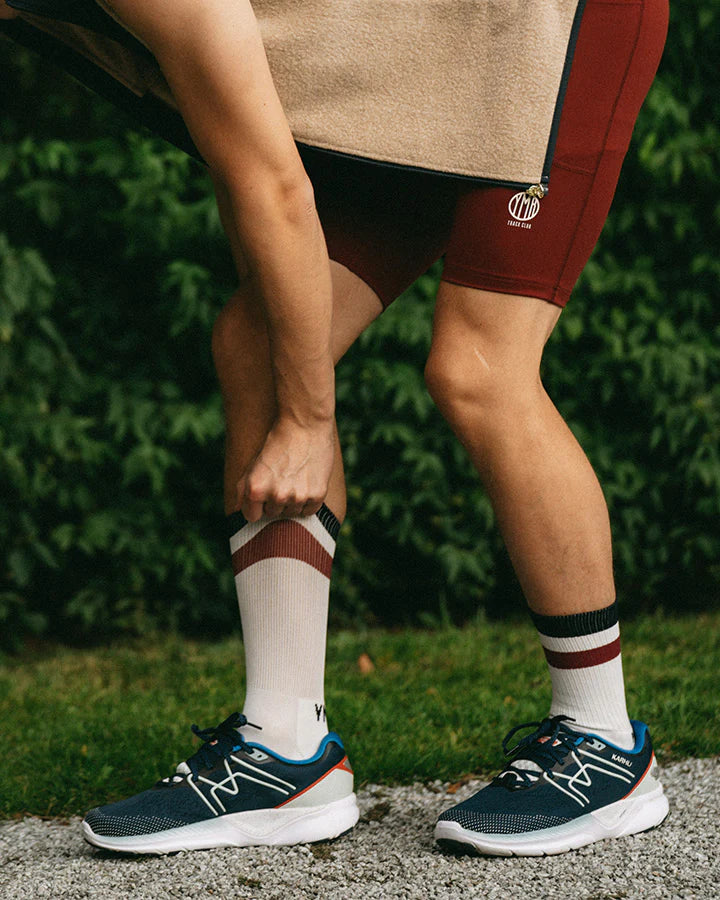 YMR Åsunden Mid Crew Socks. Vita strumpor med en röd och en blå rand upptill. Text "YMR TC" ovanför hälen. Extra vaddering under foten och vid hälen för ökad komfort och slitstyrka vid löpning eller annan fysisk aktivitet.