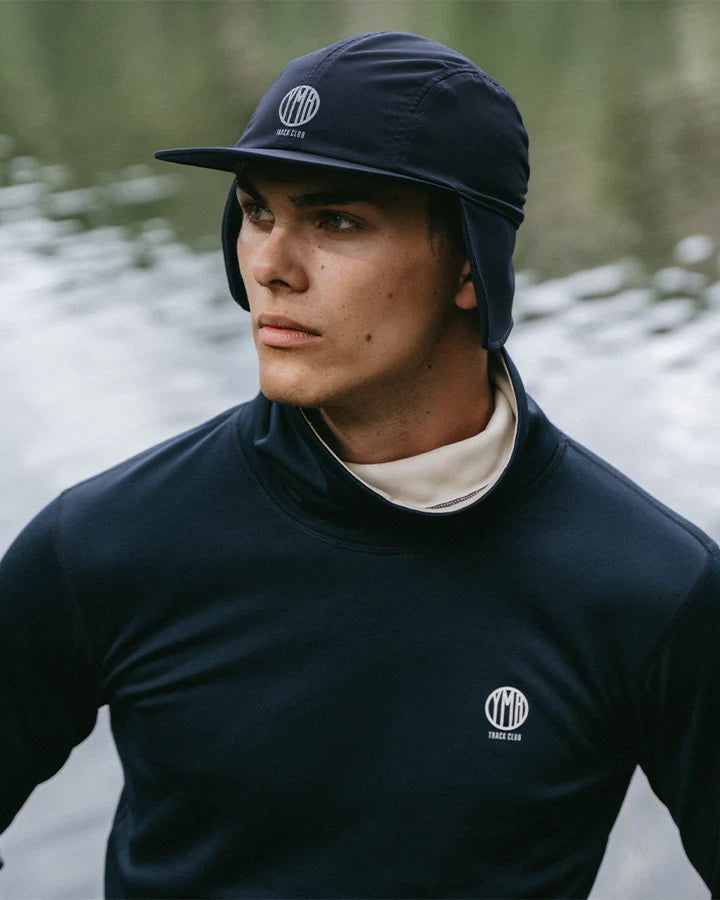 YMR Åsunden Men's Funnel Neck Navy. Mångsidig och mjuk tröja i marinblått med beige inuti den höga kragen och på logotyp på bröstet. Dragsko i både kragen för justerbar passform. Reflexdetalj på nedre delen av ryggen. 