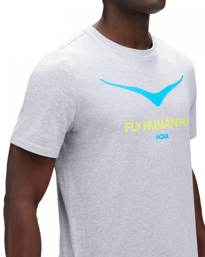 Skön grå T-Shirt med Hoka loggan i blått på bröstkorgen. Under loggan står det "FLY HUMAN FLY" i grön färg.