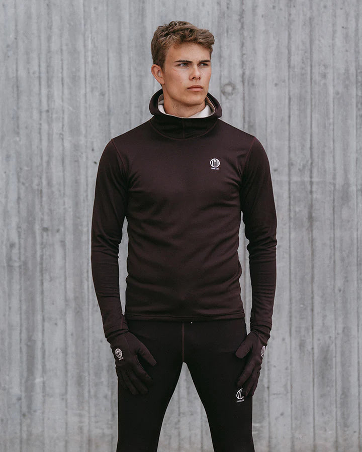 YMR Åsunden Men's Hoodie. Hoodie i rödbrun nyans med beige kontrastfärg på insidan av luvan och på loggan på bröstet. Huva med hög krage och tumöppningar i ärmsluten. Tight, sportig passform. 