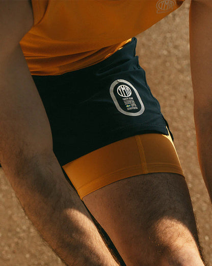 Marinblå 2-1 shorts med ett ytterlager av lätt funktionsmaterial. Under finns ett par gula kompressionstights med sidfickor på båda benen. Vit logotyp på framsidan, vänster ben. Midjebandet säkras med invändig snörning. 