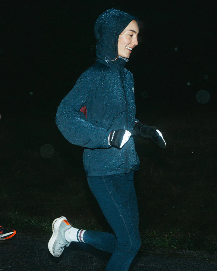 Vind- och vattenavvisande mörkblå löparjacka för dam med huva och ventilation.
Ventilation i stickad mesh under armarna, dragskojusterbar huva som kan rullas in i kragen, samt dragkedjeförsedda sidfickor för förvaring. Jackan pryds av YMR:s logotyp i off-white framtill och ett reflexprint i svanken för ökad synlighet i mörker. Logga i Offwhite och vinrött på ryggen. Mudd i ärmslut i vitt och vinrött. Dragsko i midjan.