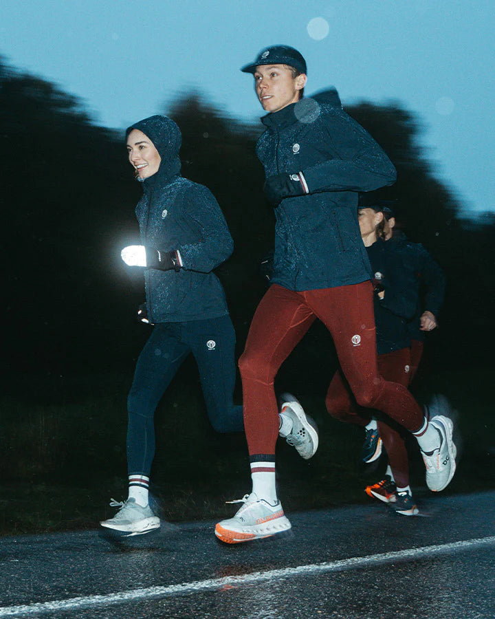 Vind- och vattenavvisande mörkblå löparjacka för herr med huva och ventilation.
Ventilation i stickad mesh under armarna, dragskojusterbar huva som kan rullas in i kragen, samt dragkedjeförsedda sidfickor för förvaring. Jackan pryds av YMR:s logotyp i off-white framtill och ett reflexprint i svanken för ökad synlighet i mörker. Logga i Offwhite och vinrött på ryggen. Mudd i ärmslut i vitt och vinrött. 